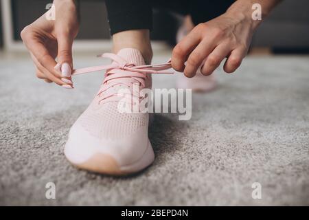 Close up of sporty sneakers on which young girl tying laces. Active woman preparing for morning exercise at home. Concept of regular training. Stock Photo