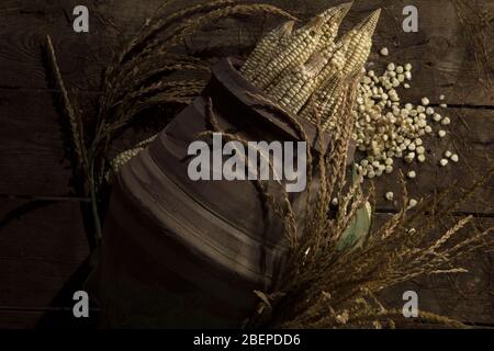 Top view of pot with fresh corn. Ears of corn in jar with wheat classes on wooden floor with scattered corn kernels. Stock Photo