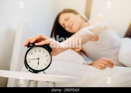 Alarm clock ringing,annoyed woman waking up in early morning for work.Sleeping disorder.Tired woman oversleeping,bad sleep quality.Sleep deprived.Bad Stock Photo