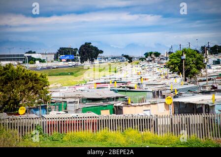 Township shacks in Khayelitsha on the edge of Cape Town. Satellite dishes are common and most shacks have electricity. The motorway to the airport passes nearby. The vegetation is lush. Stock Photo