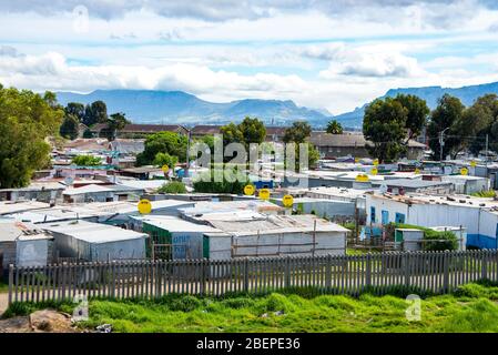 Township shacks in Khayelitsha on the edge of Cape Town. Lush mountains rest in the background. Satellite dishes are common and most shacks have electricity. Stock Photo