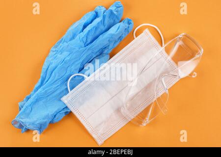Satety glasses, medical mask and protective gloves on orange background. Top view Stock Photo