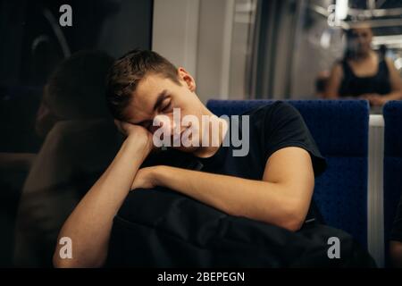 Passenger sitting in the seat and sleeping inside a train/bus while traveling.Tired exhausted looking young man getting away with train ride. Stock Photo