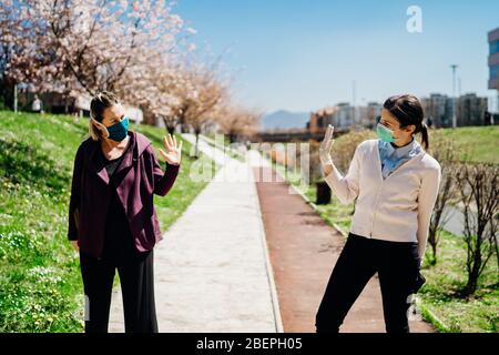 Two friends with protective masks greet with waving to each other.Alternative greeting during quarantine to avoid physical contact.Coronavirus COVID-1 Stock Photo