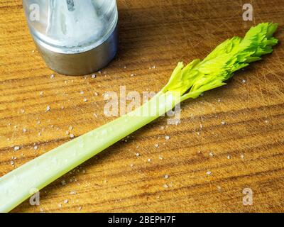 A single stick of celery on a wooden board with freshly milled sea salt and a salt mill Stock Photo