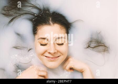 young woman taking a bath in milk - happy with closed eyes - self care and wellbeing concept