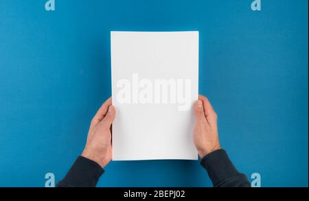 directly above shot of hands holding white blank sheet of paper against blue desk background template Stock Photo