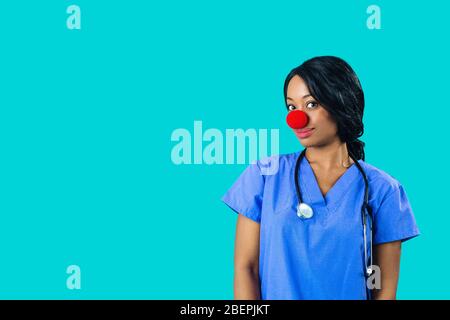 Portrait of a smiling female doctor or nurse wearing blue scrubs uniform and red nose looking at camera isolated on blue background Stock Photo