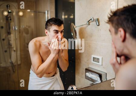 Young man having a shaving daily beard grooming routine,applying aftershave lotion.Allergic itchy rash burn reaction to hygiene skin care product.Faci Stock Photo