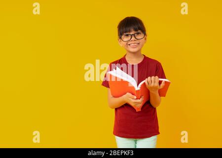 Young Asia girl student with big smiled wearing glasses and red shirt open and read  book on yellow background in studio Stock Photo
