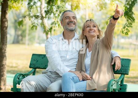 Happy senior couple sit and point to look in park with big smiled Stock Photo