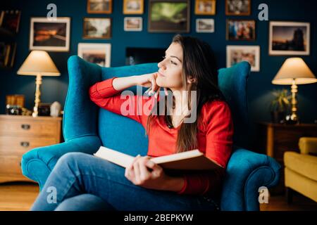 Woman thinking while reading a book at home,being distracted by her thoughts.Concentration problems.Bibliotherapy.Therapeutic literature.Attention dis Stock Photo
