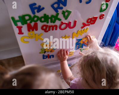 Two children learn the alphabet with magnetic letters one a fridge at home Stock Photo
