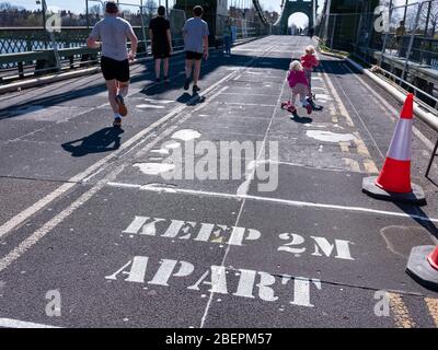 A sign painted on the road surface warns pedestrians to keep their distance in order to prevent the Covid 19 virus spreading. Hammersmith Bridge, Lond Stock Photo