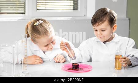 Boy and girl in white coats perform chemical experiments in an entertaining way, investigating the reaction of substances Stock Photo