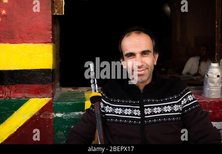 A local man holding a shisha pipe and smiling at a cafe in downtown Amman, Jordan Stock Photo