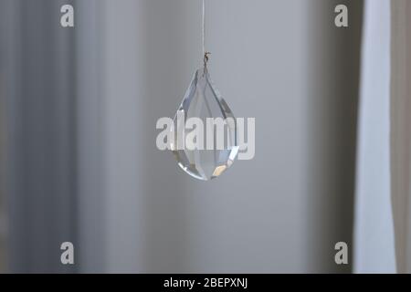 Close-up on drop-shaped glass decoration crystal hanging on the string, viewed against grey blurred background with copy space Stock Photo