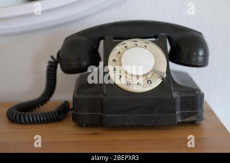 Black vintage landline phone device with rotary dial and coiled cord, sitting on lacquered wooden table, viewed from the front in close-up Stock Photo