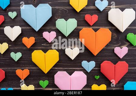 Origami hearts of different colors and sizes in composition on weathered black wooden background Stock Photo