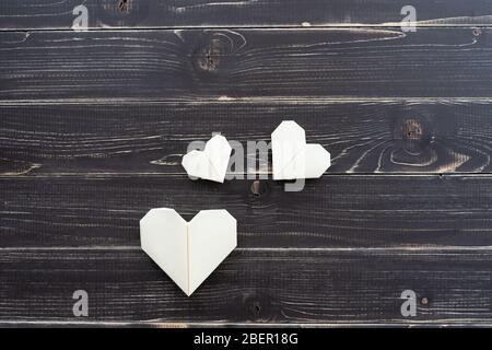 Origami hearts of different colors and sizes in composition on weathered black wooden background Stock Photo