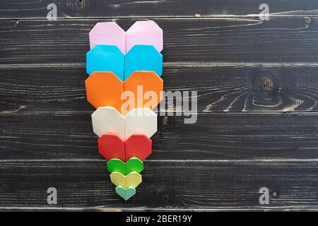 Origami hearts of different colors and sizes in composition on weathered black wooden background Stock Photo