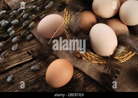 Easter composition in vintage style - wicker basket with eggs, feathers and willow cats on a burlap sack and a wooden table Stock Photo