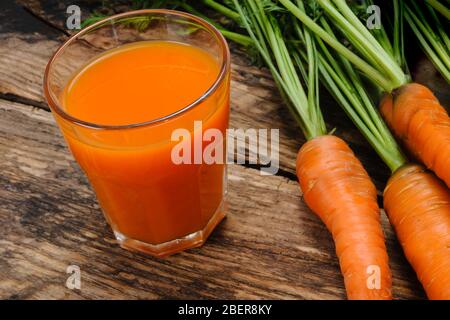 Glass of fresh carrot juice and bunch of raw organic carrots on a wooden rustic table Stock Photo