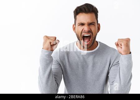 Champion, sport and bid concept. Good-looking energized and excited handsome guy triumphing, shaking clenched fists as celebrating victory Stock Photo