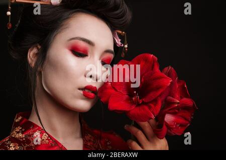 Image of beautiful geisha woman in traditional japanese kimono holding flowers isolated over black background Stock Photo