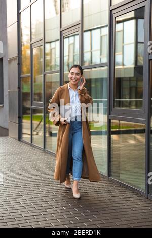 Image of young brunette asian woman wearing earbuds holding laptop computer while walking through city street Stock Photo