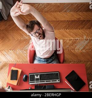 Man is resting, yawns and stretches, working remotely on his computer at home. Concept of quarantine during a virus outbreak. Stock Photo