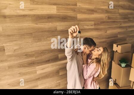 Cheerful girl and happy man moving to new apartment with cardboard boxes and beautiful flowers. Stock Photo