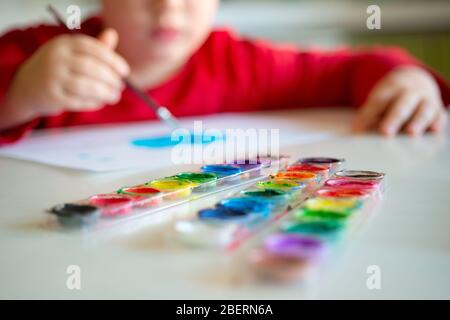 Boy Learns to Paint with a Brush on Paper Sitting at a Table Stock Photo