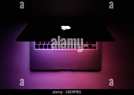 a macbook half closed with purple glow in the dark Stock Photo