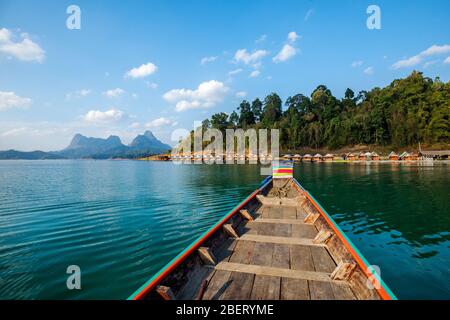 Wooden traditional Thai longtail boat on Cheow Lan lake arriving at floating bungalow huts in Khao Sok National Park, Thailand