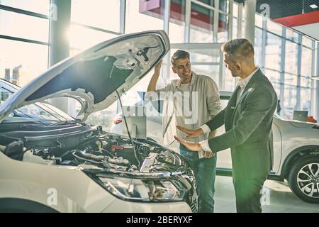 A smiling buyer checking an engine part of new car. Stock Photo