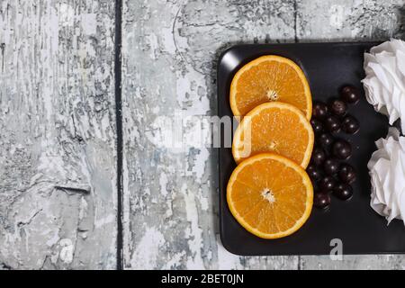 orange slices and candy on a black plate on a wooden background Stock Photo