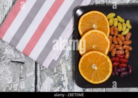 orange slices and candy on a black plate on a wooden background Stock Photo