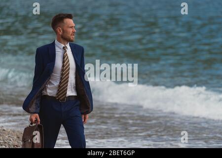 Businessman walking on the beach holding in hand briefcase Stock Photo