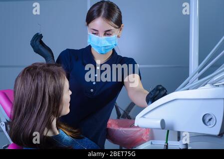 a dentist in a mask and gloves, shows a happy patient an x-ray of the teeth, telling her about the pathology of the tooth. In the dental office, again Stock Photo