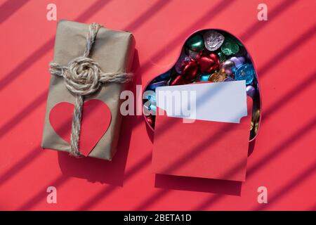 close up of candy in a heart shape box and envelope on red background  Stock Photo