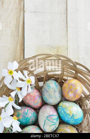 Coconut sticks plate with colorful Easter eggs and  Poets Narcissus flowers on wooden table Stock Photo