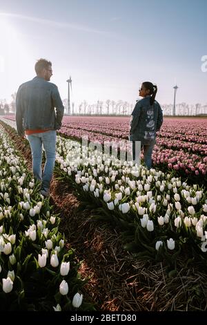 Tulip flower field during sunset dusk in the Netherlands Noordoostpolder Europe, happy young couple men and woman with dress posing in flower field in