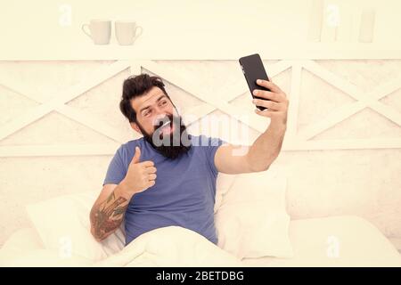 Just thumb up. Happy hipster give thumb up to phone camera. Bearded man smile with thumb up and smartphone. Gesturing satisfaction. Thumb up for new technology. Mobile lifestyle. Modern life. Stock Photo