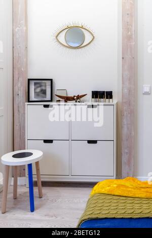 Detail of a bedroom of a modern studio apartment in the attic of the old house. Part of the bed, stool, chest of drawers, a mirror on the wall Stock Photo