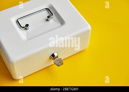 Close up of small white closed cashbox or money box with key in lock on yellow background with copy space Stock Photo
