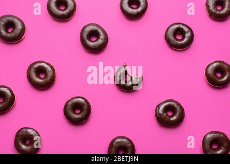 Doughnuts aligned symmetrically on a pink background. Chocolate donuts pattern, one with a missing bite. Delicious donuts background. Unhealthy eating Stock Photo