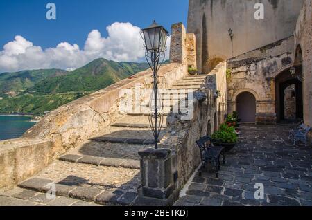 Courtyard old medieval knight's castle on rock Castello Ruffo with stone ancient walls, street lamp, vases with flowers and blue sky background, Scill Stock Photo