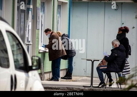 Sofia, Bulgaria. 15 April 2020. Unemployed people wearing protective face masks waiting and filling out forms on impromptu social distancing small tables outside a local job centre of the Department for Social Protection. The unemployment in the country has risen to 7% because of the Pandemic Coronavirus Covid - 19 after years of stable low rates at around 3.5%. Stock Photo