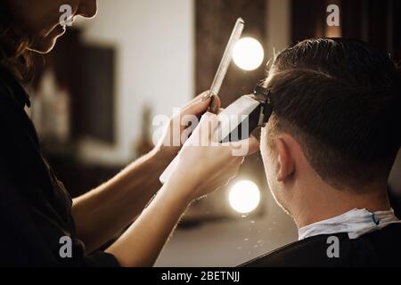 Close up view of hairdresser cutting hair of man in barbershop. Stock Photo